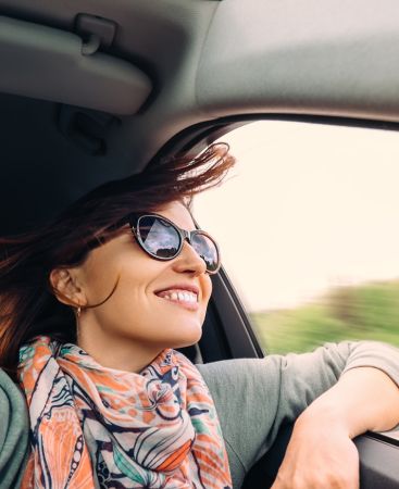 Mujer joven de 25 a treinta años con jersey azul y pañuelo conduciendo su coche y contenta de no detenerse en el peajes con el Vía-T de Creand
