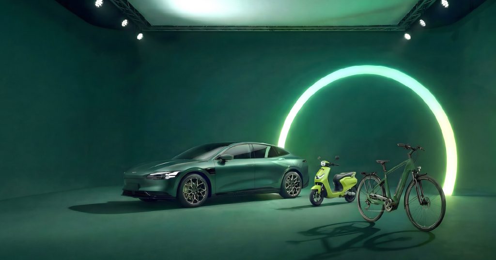 Cotxe elèctric junt una bicicleta elèctrica i una moto elèctrica, sobre un plató verd i amb un aro de llum verda al fons.