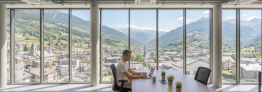 Home treballant a una oficina oberta, estil coworking. De fons es veu Andorra la Vella.